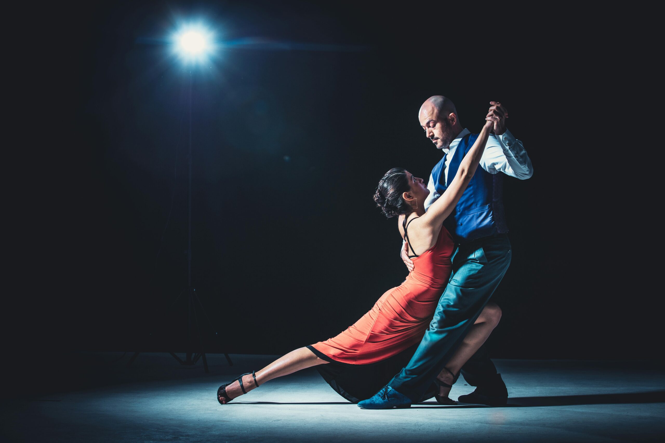 Elegant couple performing tango under a dramatic spotlight, showcasing passion and grace.